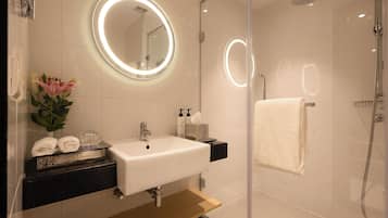 A modern bathroom with a glass-enclosed shower, a white sink, and a mirror with a circular light.