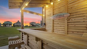 A wooden outdoor seating area with a sign reading "Corona." - Steps to the Beach • Hot Tub • Modern 5★ Crystal Beach Getaway (Crystal Beach)