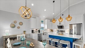 A modern kitchen with white cabinets, a blue island, stainless steel appliances, and hanging wicker pendant lights. - Steps to the Beach • Hot Tub • Modern 5★ Crystal Beach Getaway (Crystal Beach)