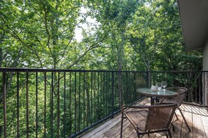 En balkon med et rundt bord og fletstole, med udsigt over en tæt skov.