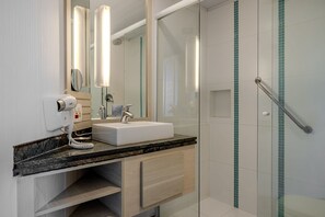 A modern bathroom with a white sink, a hairdryer, and a glass shower enclosure. - Vossa Bossa Flat Jardins (São Paulo)