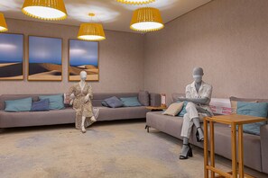 Et moderne værelse med en grå sofa, et træsidebord og en mannequin klædt i en hvid frakke.