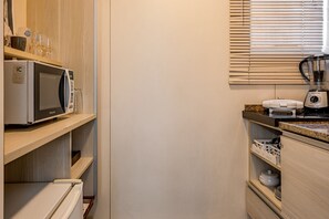 A compact kitchen with a microwave, toaster, and blender on the countertop, and a refrigerator below. - Vossa Bossa Flat Jardins (São Paulo)