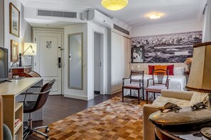 A hotel room with a desk, office chair, sofa, and armchair. There is a large window with a cityscape view. - Vossa Bossa Flat Jardins (São Paulo)