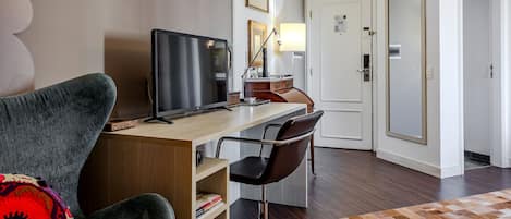 A hotel room with a desk, computer, chair, and a patterned rug.