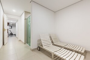 A hallway with a white wall, a glass door, and a white bench with wheels.