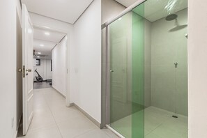 Un pasillo que conduce a un área de ducha con paredes de vidrio y ducha suspendida del techo.