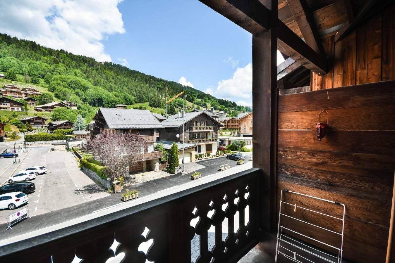 A balcony with a view of a mountain village, wooden buildings, and parked cars.