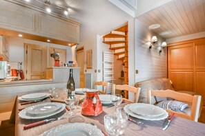 A dining area with a wooden table set for four, surrounded by wooden chairs. A spiral staircase is visible in the background, leading to an upper level.