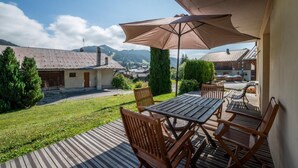 Un patio al aire libre con una mesa y sillas, un paraguas grande y vistas a un pueblo y montañas al fondo.