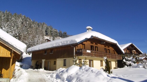 Una cabaña de madera con balcón, rodeada de árboles nevados y un cielo azul despejado.