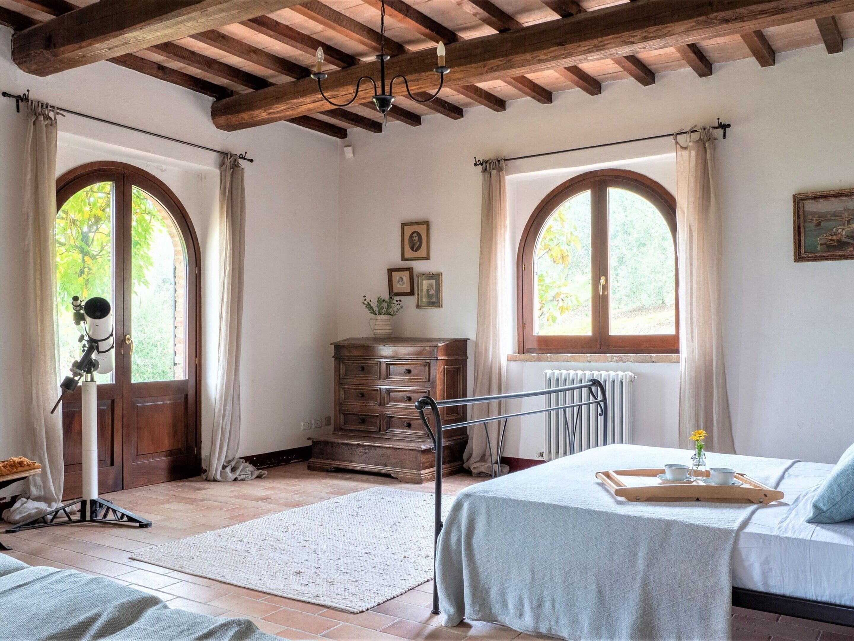 A bedroom with a bed, a dresser, a telescope, and a window with curtains.