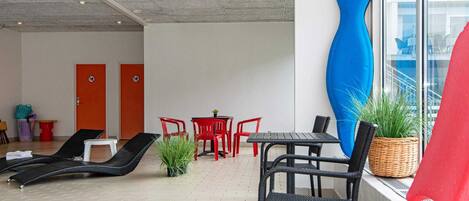 A modern lounge area with red and black chairs, a small table, and a large blue sculpture.