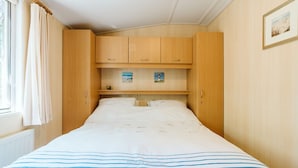 A bedroom with a bed, wooden wardrobe, and a shelf with pictures. - Detached Chalet With a Panoramic View! (Goedereede)