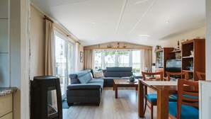 A modern living room with a sofa, dining table, and chairs. There is a television and a fireplace. - Detached Chalet With a Panoramic View! (Goedereede)