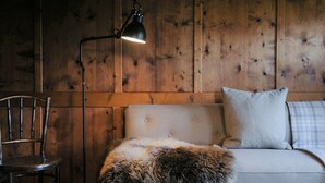 A cozy room with a wooden wall, a sofa with a fur throw, a lamp, and a chair. - Chalet in Montafon With Private Sauna & Views (Vandans)