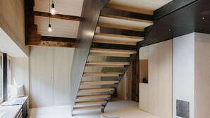 A modern interior with a wooden staircase, a black sofa with cushions, and a window with a view. - Chalet in Montafon With Private Sauna & Views (Vandans)