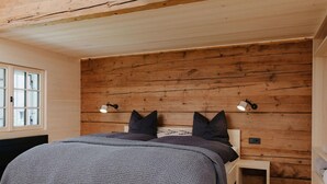 A bedroom with a wooden headboard, a bed with a grey knitted blanket, two bedside lamps, and a small bedside table. - Chalet in Montafon With Private Sauna & Views (Vandans)