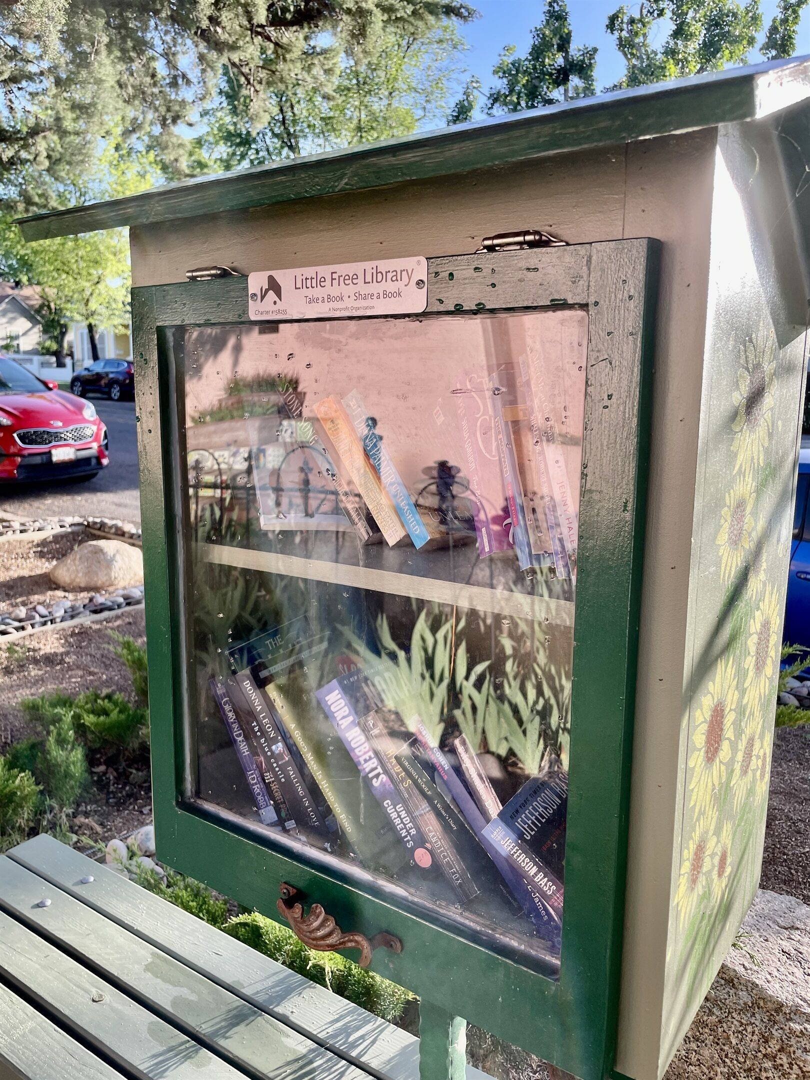 A Little Free Library box with books inside, located outdoors with a bench nearby.