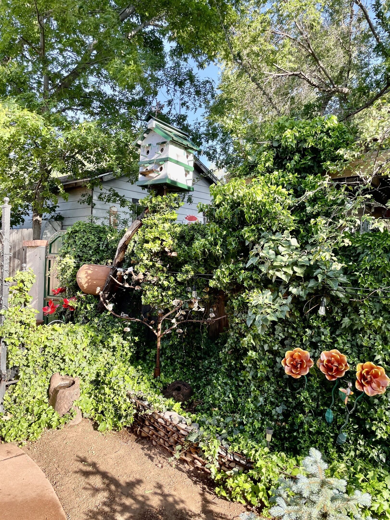 Un jardin agrémenté d’une nichoir, d’une clôture en bois et d’une variété de plantes et de fleurs.