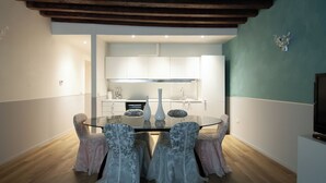 A dining area with a glass table, chairs, and a kitchen in the background.