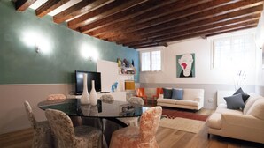 A living room with a glass dining table, chairs, a sofa, and a television.