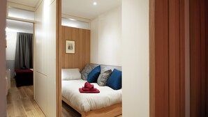 A modern bedroom with a bed, wooden panel walls, and a small bedside table.
