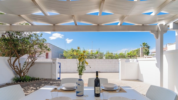 An outdoor dining area with white tables and chairs, a bottle of wine, and a vase with flowers. - 3917 Villetta Giardino dei Pini by Barbarhouse (Alliste)
