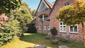 Ein zweistöckiges Backsteingebäude mit Balkon, umgeben von einem gepflegten Rasen und einem Sitzbereich im Freien.