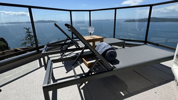 Een balkon met een metalen stoel, een klein tafeltje en een glas water. Vanuit het balkon is er een prachtig uitzicht over de zee en het landschap.