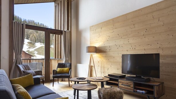 Ett modernt vardagsrum med en soffa, fåtöljer, en tv och en väggpanel av trä.