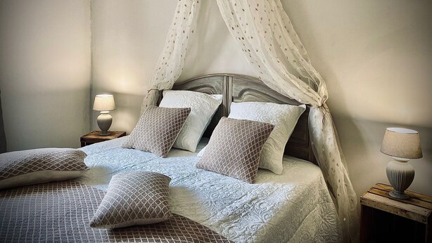 A bedroom with a canopy bed, a nightstand with a lamp, and a bedside table with a lamp. - Le Cottage du Brask (La Motte-du-Caire)