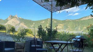 An outdoor seating area with a table and chairs, a grill, and a view of a mountain range. - Le Cottage du Brask (La Motte-du-Caire)
