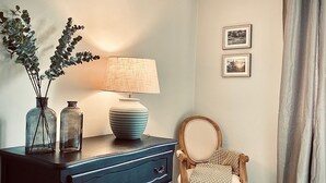A room with a dark wooden dresser, a lamp, and a chair with a woven throw. There are two framed pictures on the wall. - Le Cottage du Brask (La Motte-du-Caire)