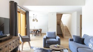 A modern living room with a TV, sofa, armchair, and coffee table. There is a dining area with a table and chairs in the background. - Wifi, sauna, hammam, terrace, balcony, parking, ski locker, 41-43m², Vaujany (Vaujany)