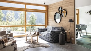 A modern living room with a large window, wooden walls, a sofa, a coffee table, and a foosball table. - Wifi, sauna, hammam, terrace, balcony, parking, ski locker, 41-43m², Vaujany (Vaujany)