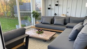 Un moderno salón con un sofá seccional gris, una mesa de centro de madera y un ventanal de vidrio que da a un jardín.