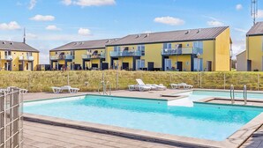En rad gula byggnader med balkonger, en swimmingpool och solstolar.