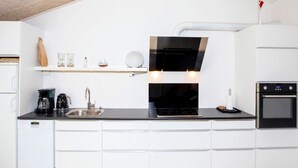 Ett modernt kök med vita skåp, en svart bänkskiva, en inbyggd ugn och en kaffebryggare.