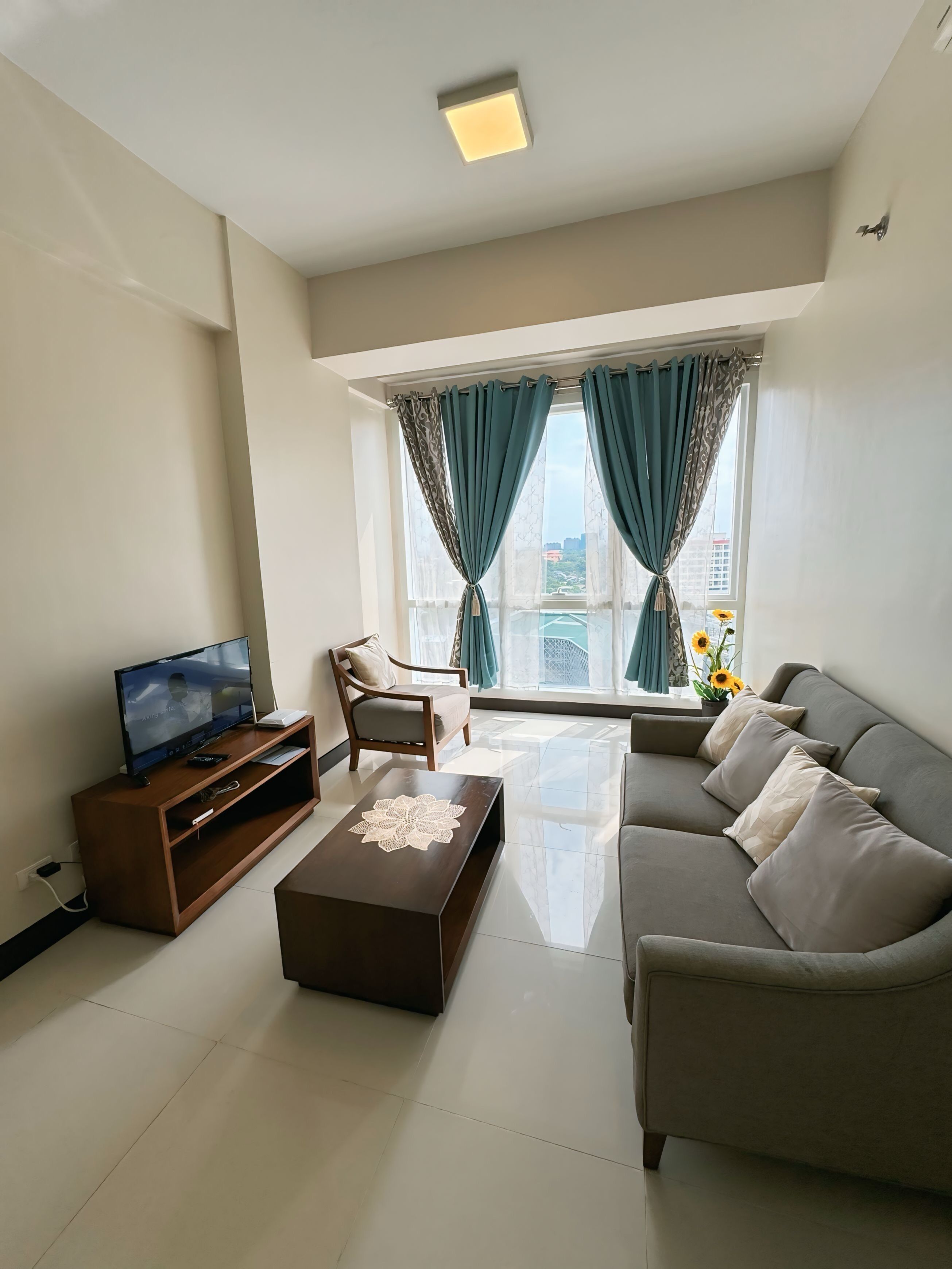 A modern living room with a sofa, coffee table, TV, and a window with curtains.