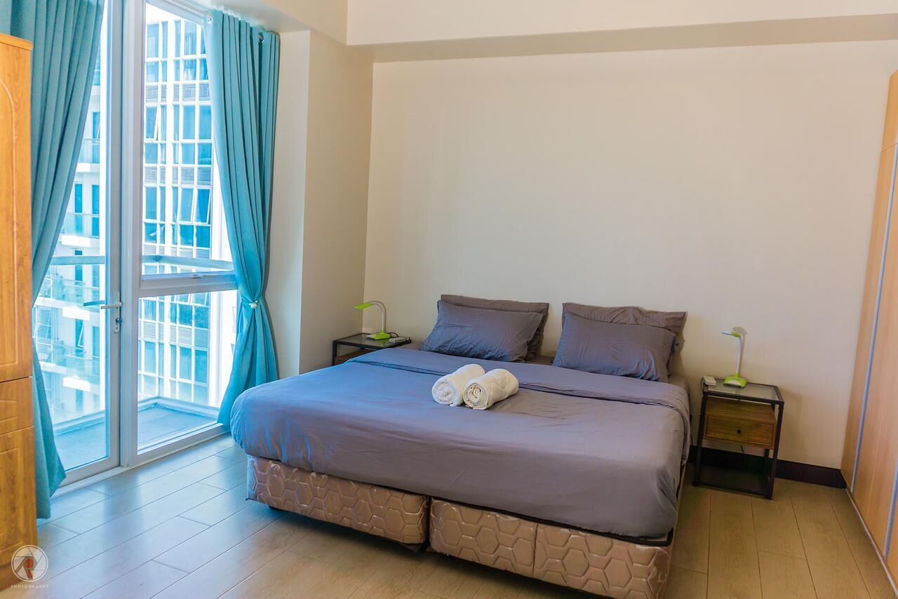 A bedroom with a bed, two pillows, a nightstand with a lamp, and a view through a glass door.