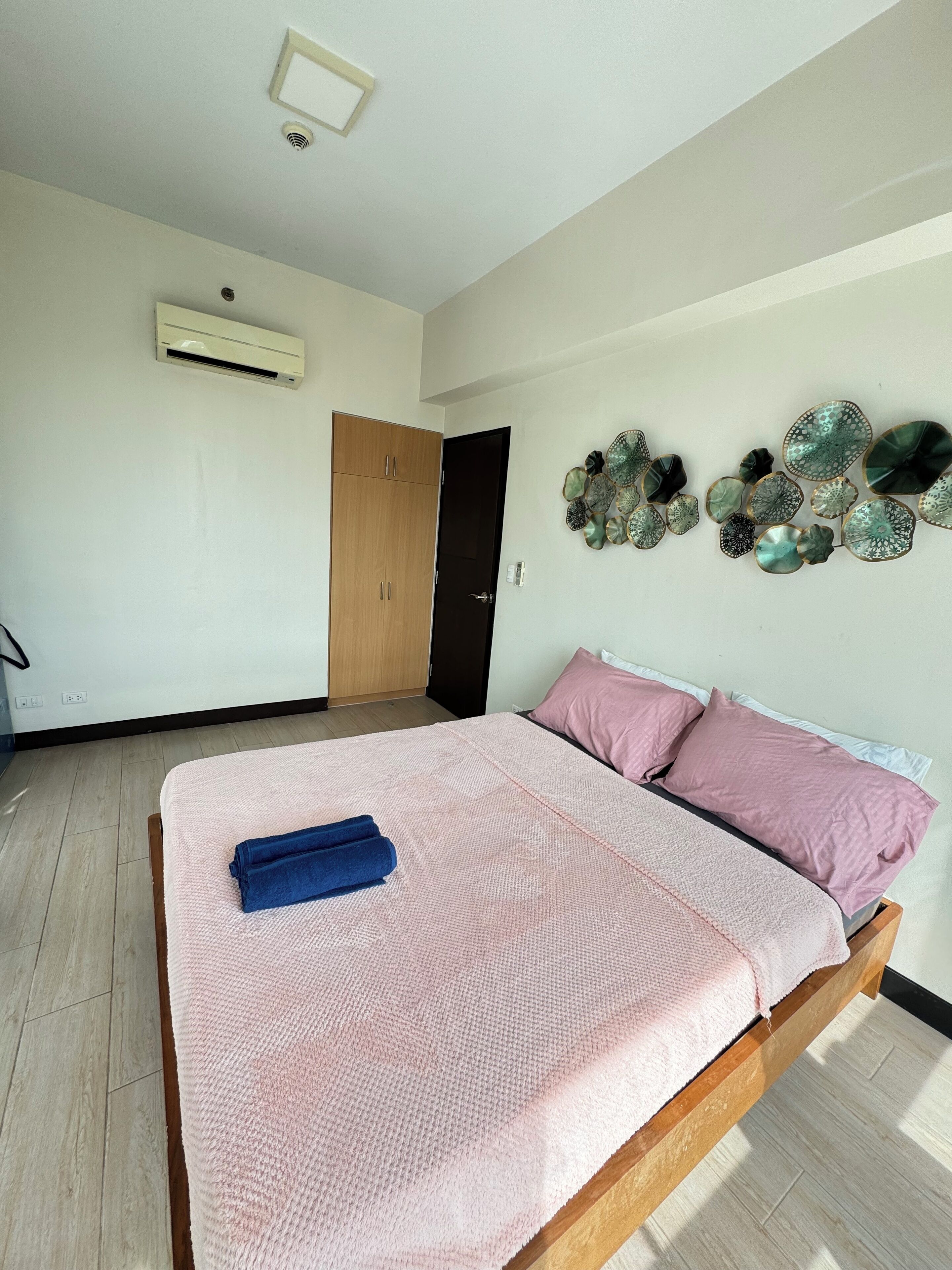 A bedroom with a bed, a wooden wardrobe, a door, and a wall-mounted air conditioning unit.