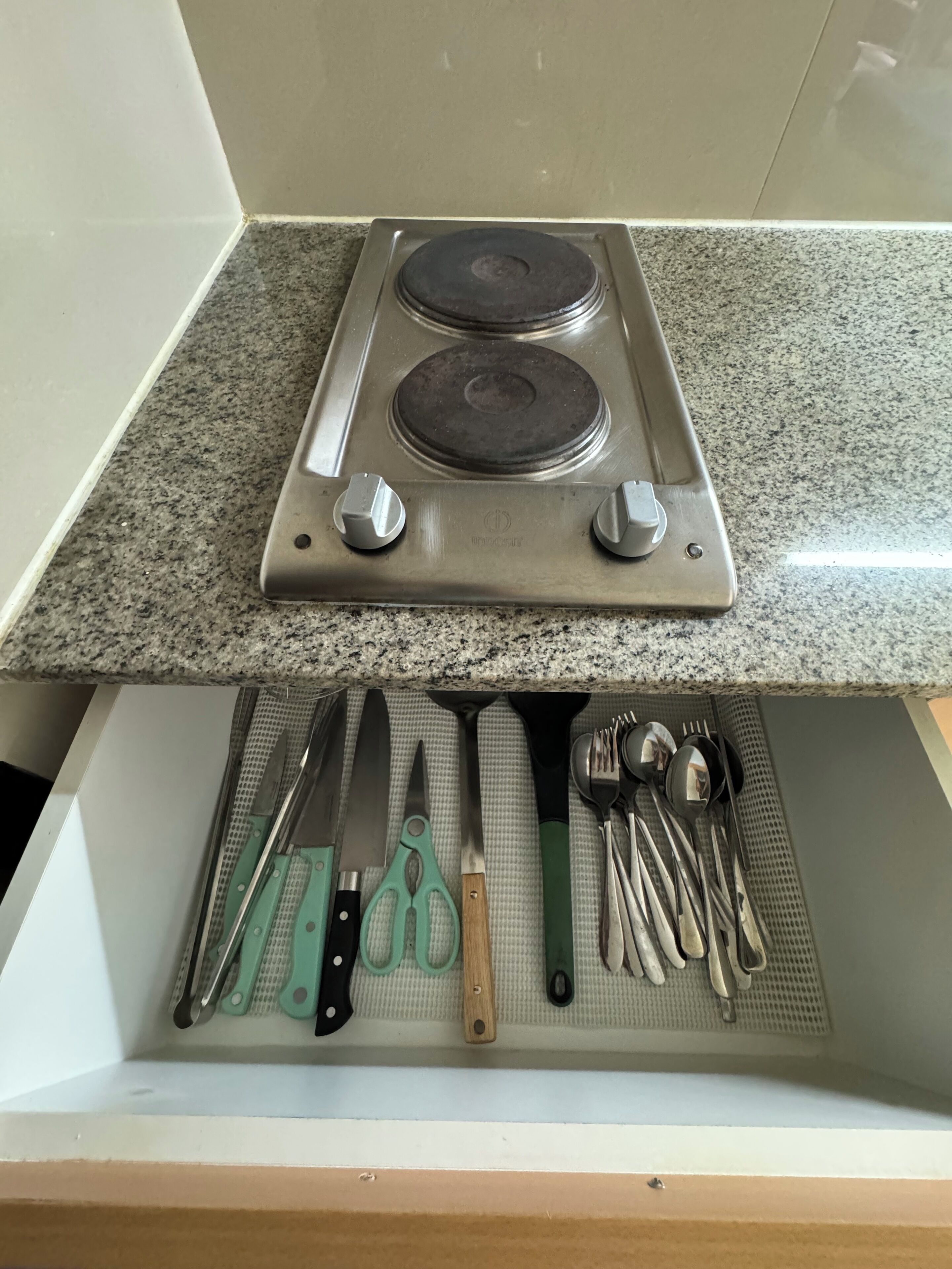 A kitchen with a granite countertop and a drawer below containing various utensils.