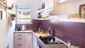 A modern kitchen with white cabinets, a purple backsplash, and a window overlooking a cityscape.