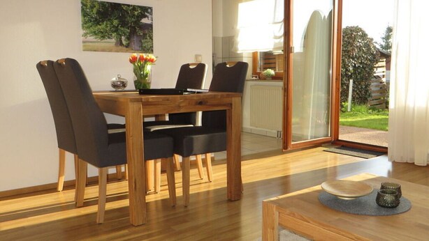A dining area with a wooden table and chairs, a vase with flowers, and a view of the outdoors through a glass door. - Holiday Apartment Borkowski (Welzheim)