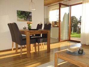 A dining area with a wooden table and chairs, a vase with flowers, and a view of the outdoors through a glass door. - Holiday Apartment Borkowski (Welzheim)