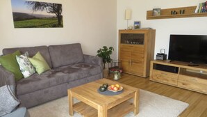 A living room with a grey sofa, a wooden coffee table with fruit, a TV, and a bookshelf. - Holiday Apartment Borkowski (Welzheim)