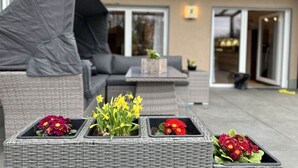 Un patio con mobiliario de mimbre, una zona de estar cubierta y macetas con flores.