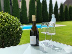 A bottle of wine and two glasses on a glass table with a pool and hedges in the background. - Cosy Apartment Near Center (Landkern)
