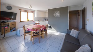 A compact living space with a dining area, kitchenette, and a large window. - Apartment Overlooking the Green Surroundings (Middelkerke)